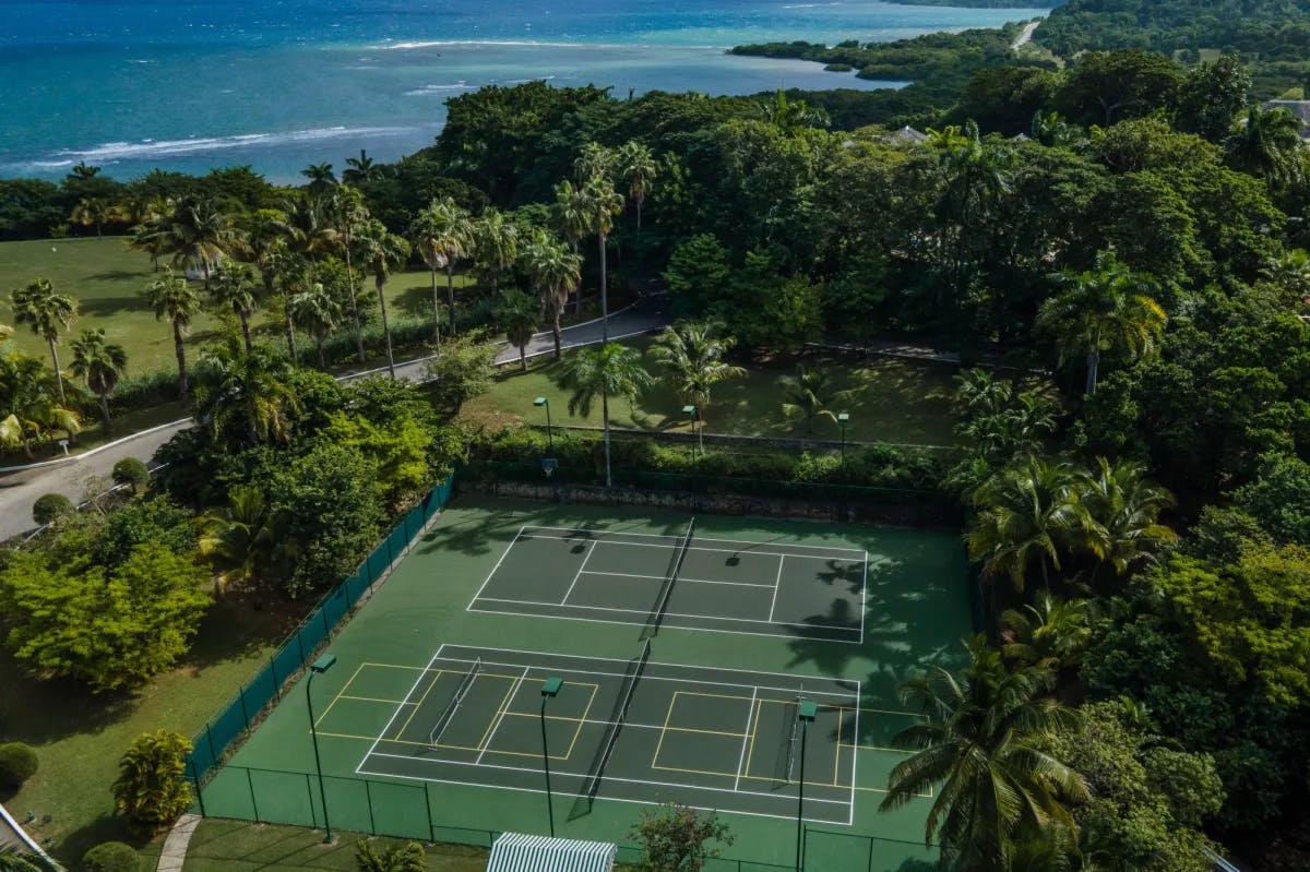 aerial view of a luxe beachside tennis court amid palm trees