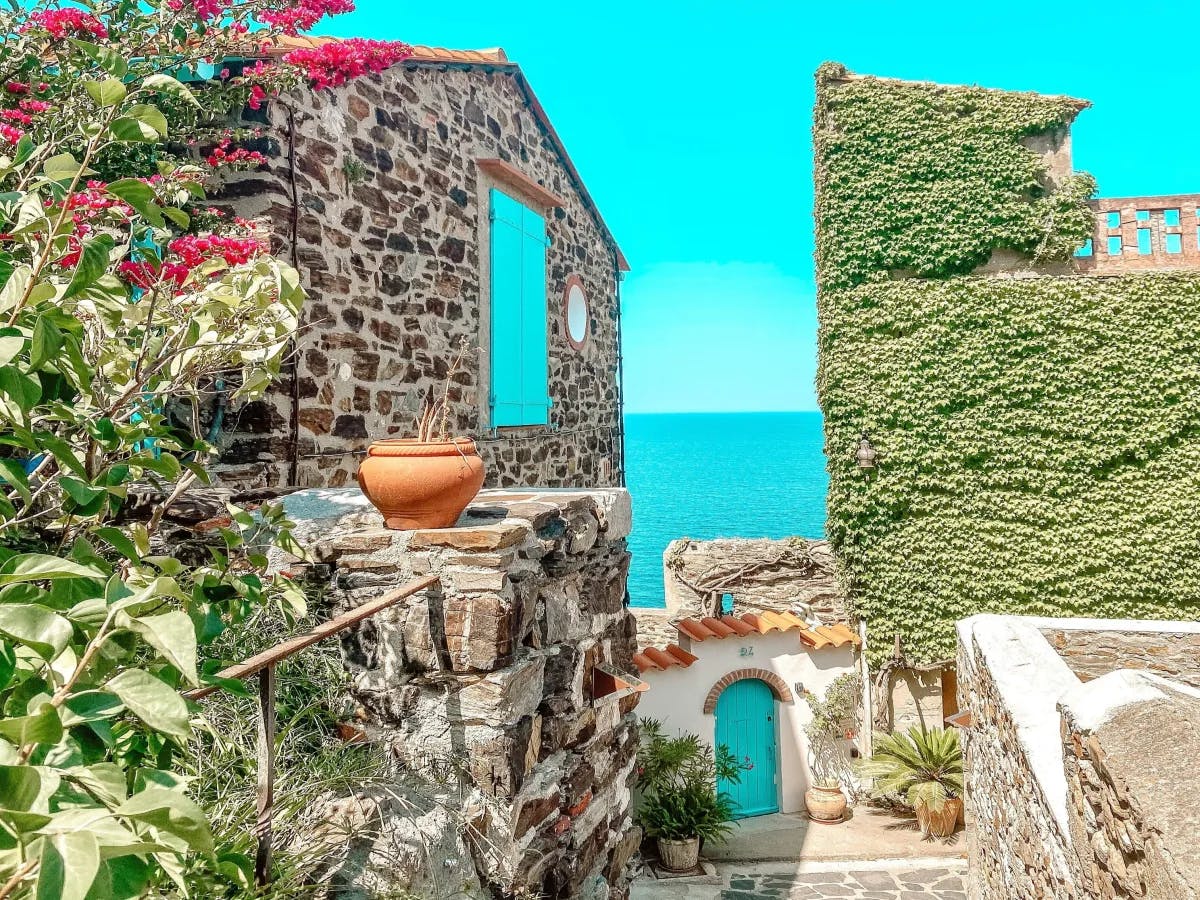 A serene coastal retreat with a stone building featuring a blue door, surrounded by lush greenery and overlooking the sea.