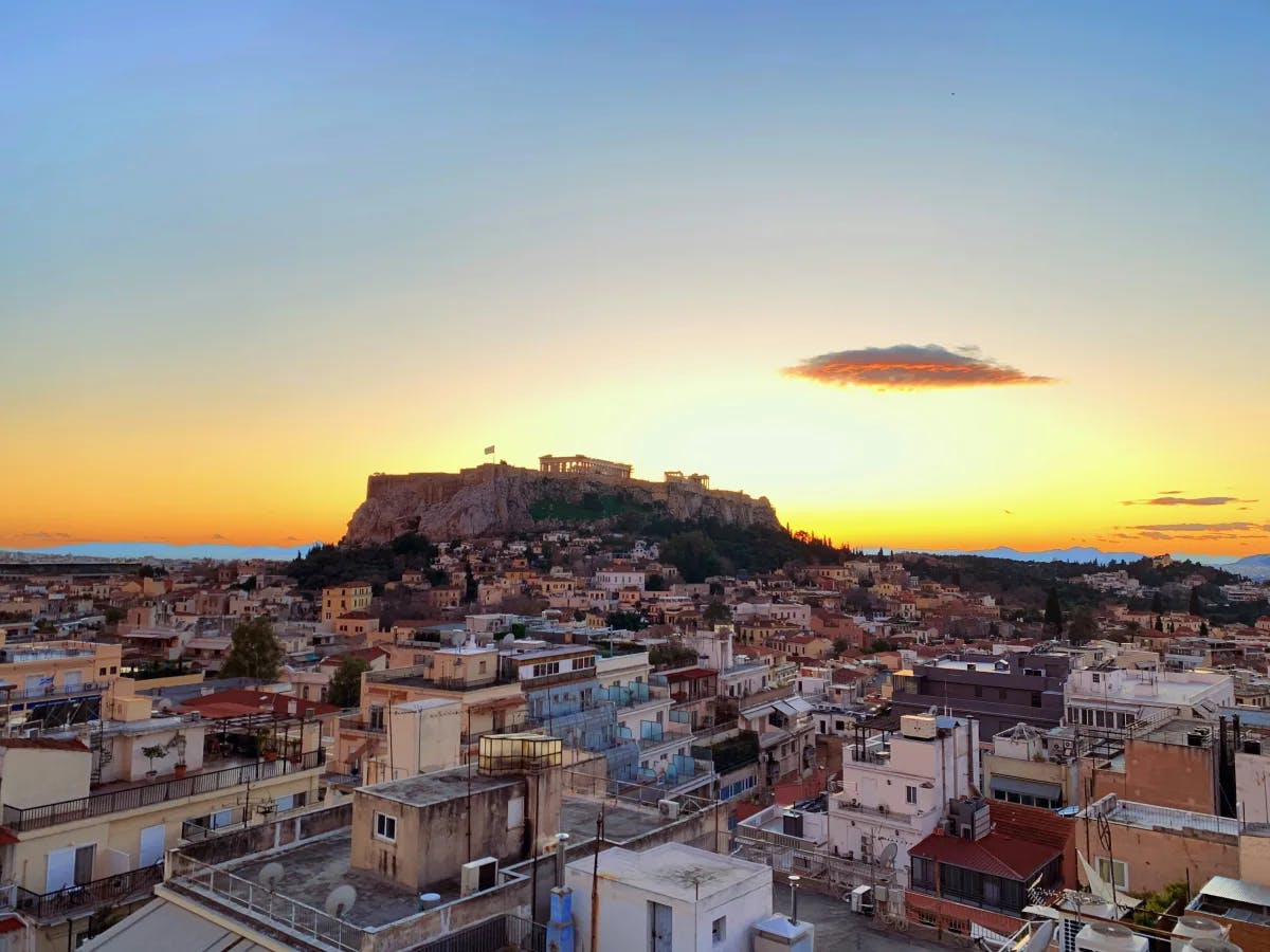 An aerial view of Athens colorful buildings at daytime. There is a golden sunset in the background. 