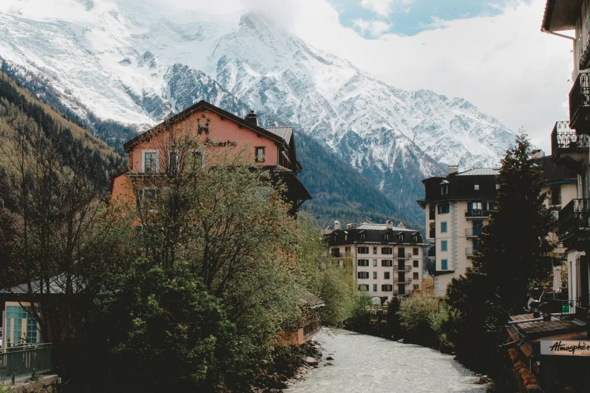 A view of a pathway, green trees and lodge-style buildings in front of a large snowy mountain.