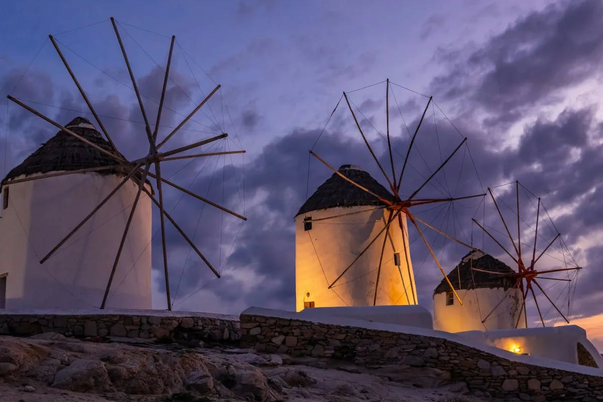 A picture of white wind turbines on brown rocky mountains under the cloudy purple sky. 