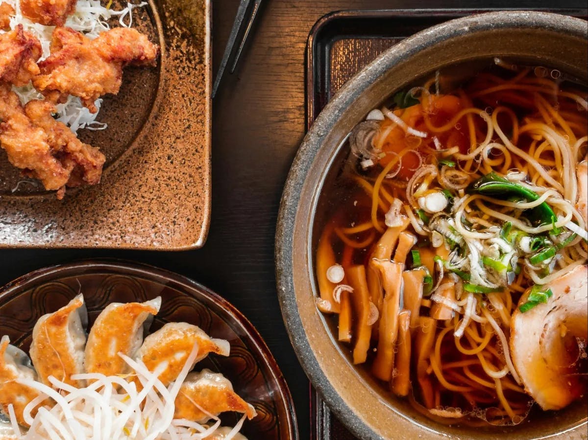 Three ceramic bowls full of Japanese food on a wooden table.