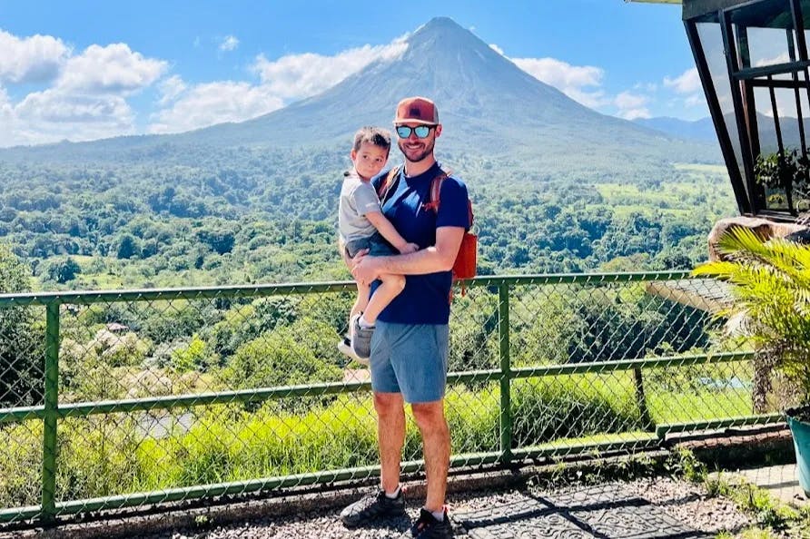 A man holding a young child in front of a beautiful vew of a forest and volcano