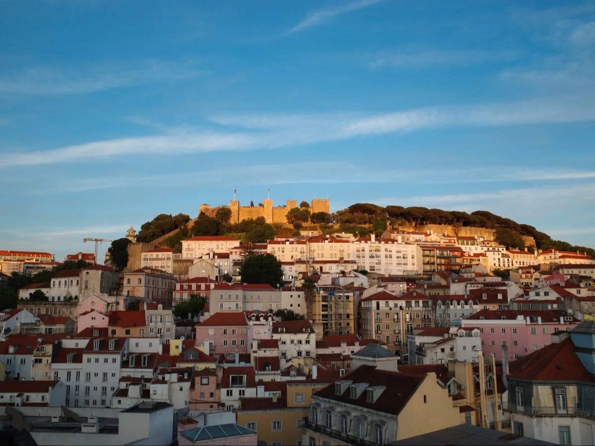 The image depicts a stunning sunset view over a city, highlighting the city’s vibrant architecture and the prominent castle on a hill.