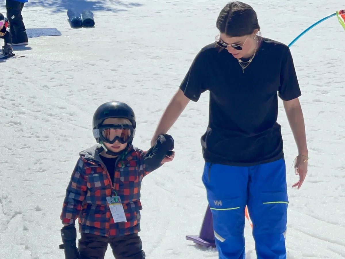 An adult ski instructor leading a small child through the snowy slopes.