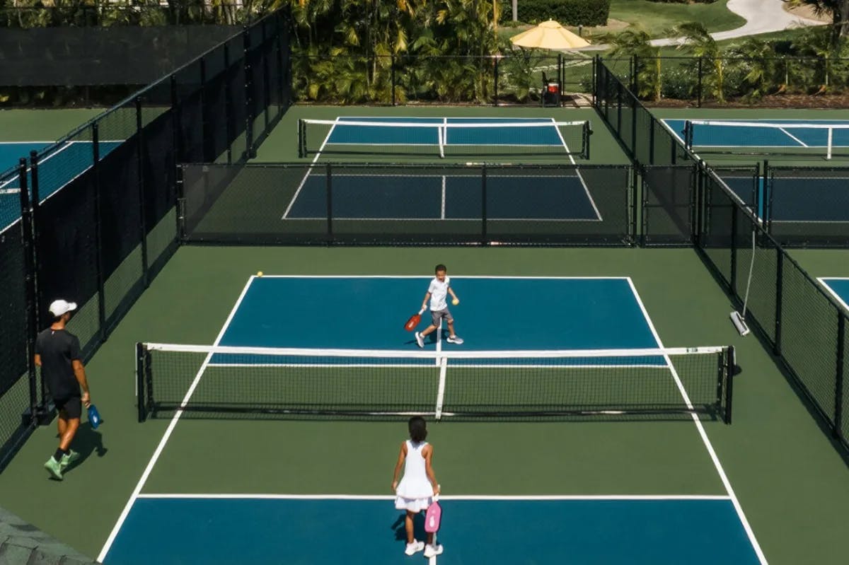 aerial view of children playing tennis on a blue-and-green court amid palm trees