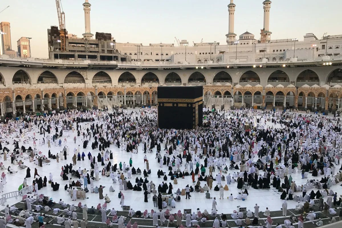 People gathered in a colosseum-type building, surrounding the Kaaba for Hajj.
