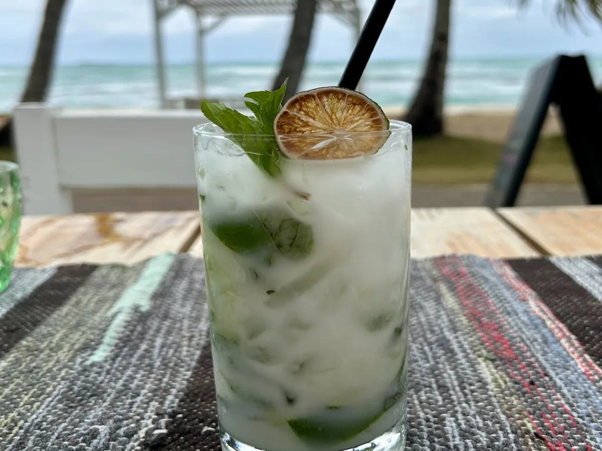 A picture of a coconut mojito on a table near the beach.