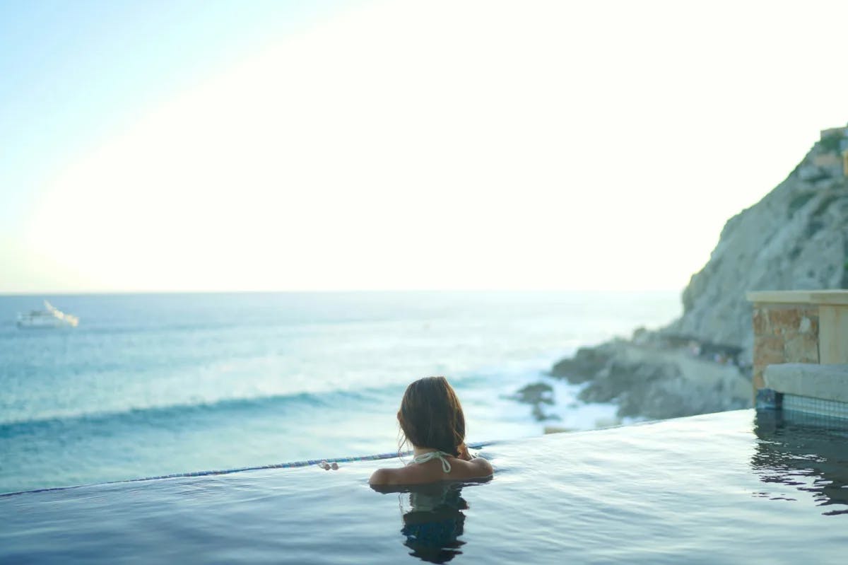 A woman in a pool facing the ocean.