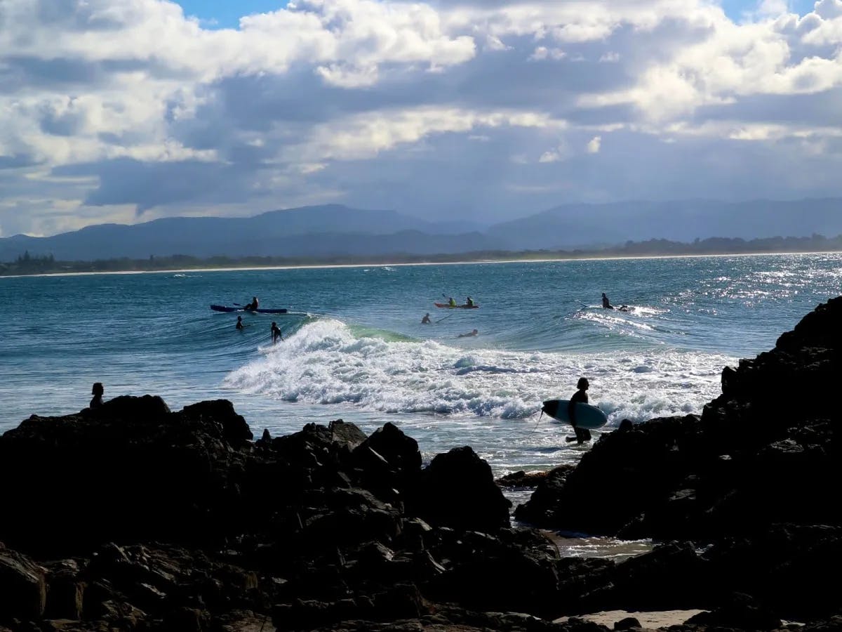 People surfing in the ocean beyond a rocky shore.