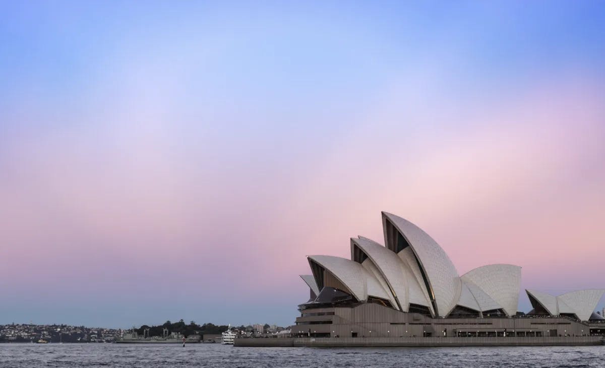 A view of the Sydney Opera House with a pink and blue sunset in the background.