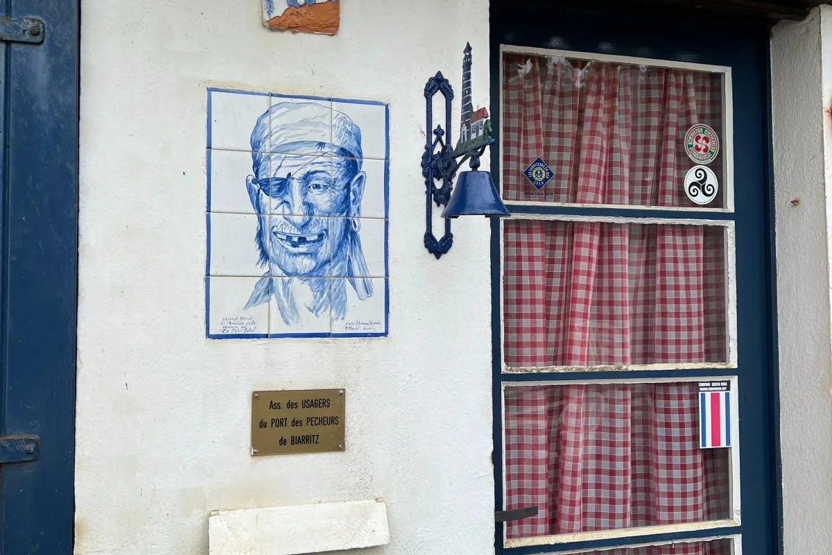 A white building with a tile portrait of a pirate next to a blue-framed building with a red and white curtain.