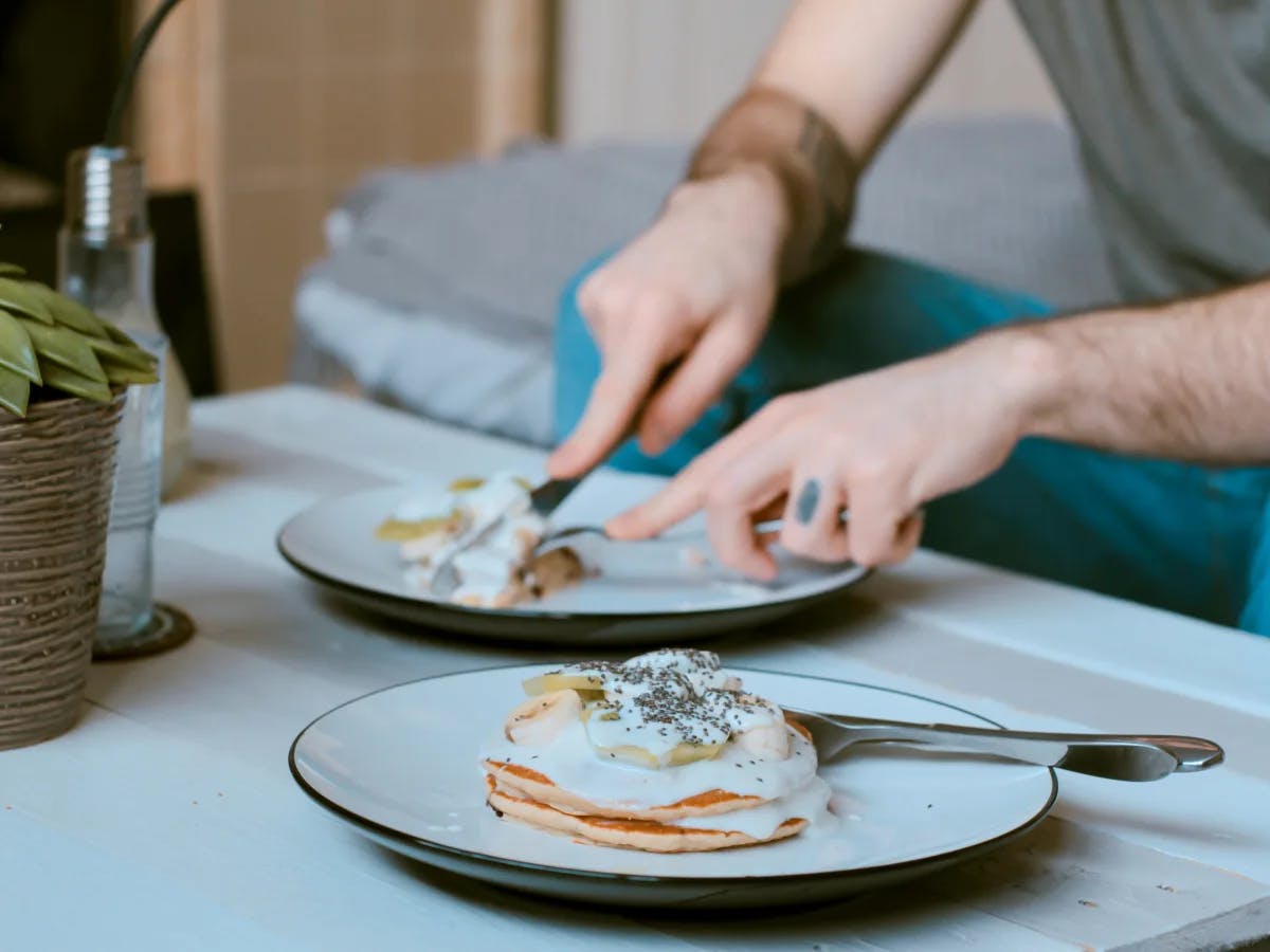 A person enjoying a meal of pancakes with toppings, seated at a table with a cozy and informal dining atmosphere.