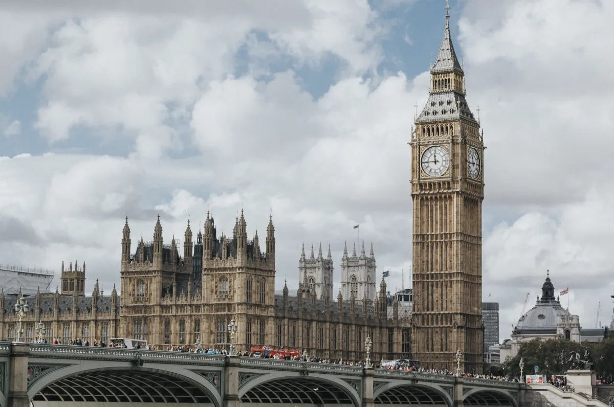 A photograph of Big Ben, a large clock tower and a bridge in London on a cloudy day. 