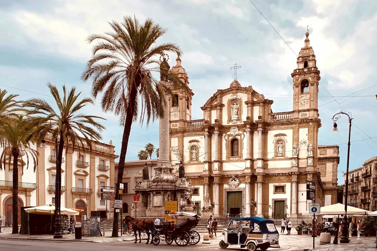 An ornate brown and white church with palm trees out front and a horse-drawn carriage.