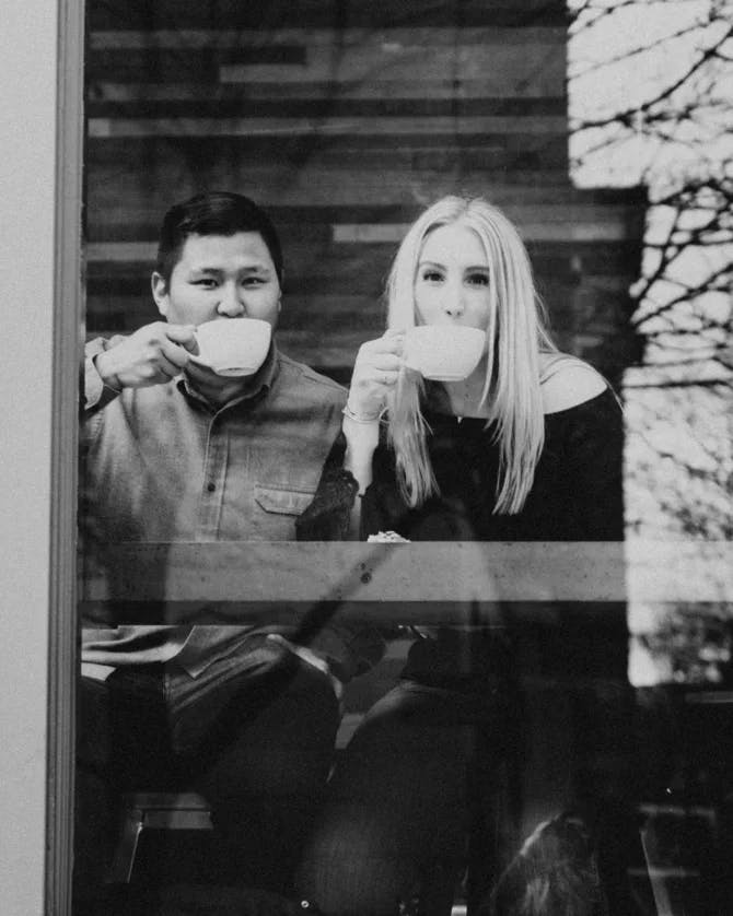 A black and white photo of two people seated inside of a cafe drinking out of a mug 