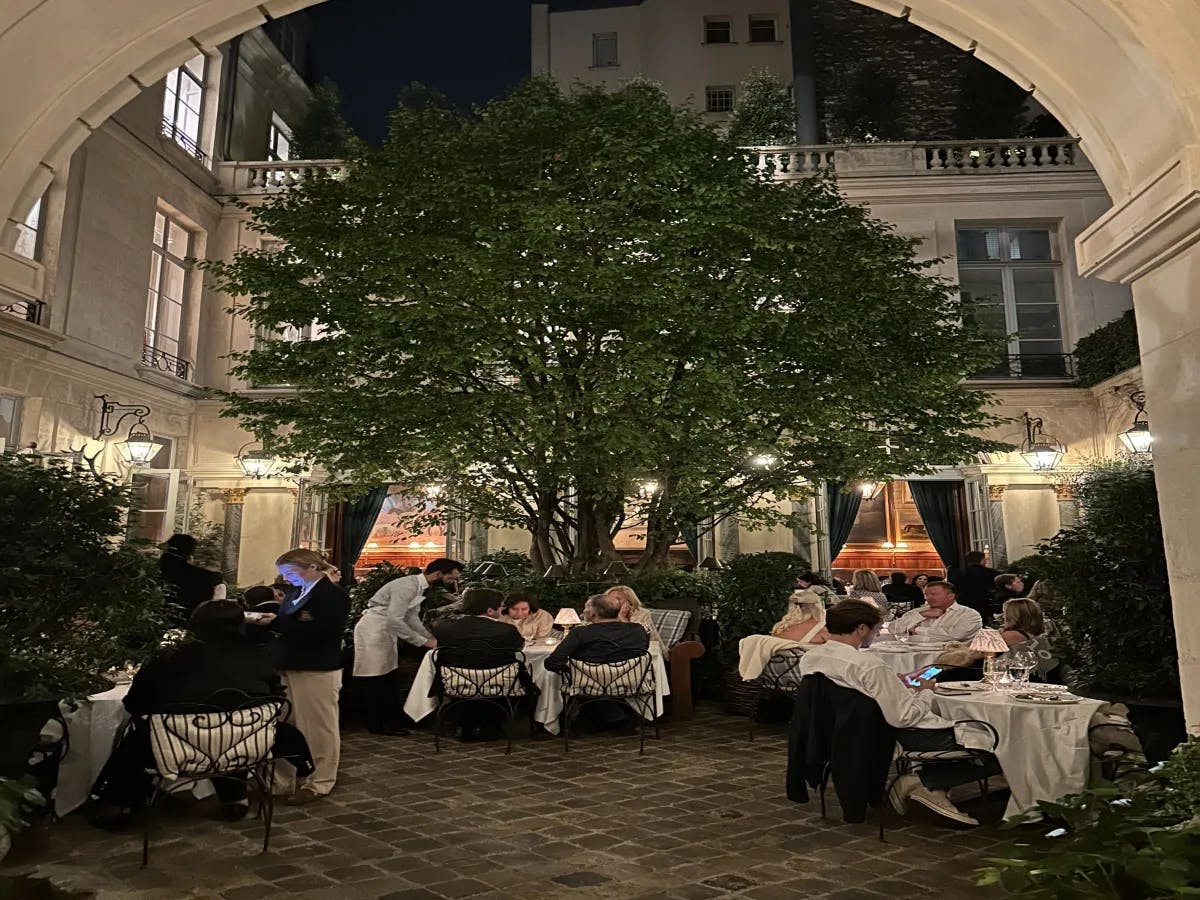 An outdoor restaurant with white-linen tables around a tree at nighttime.