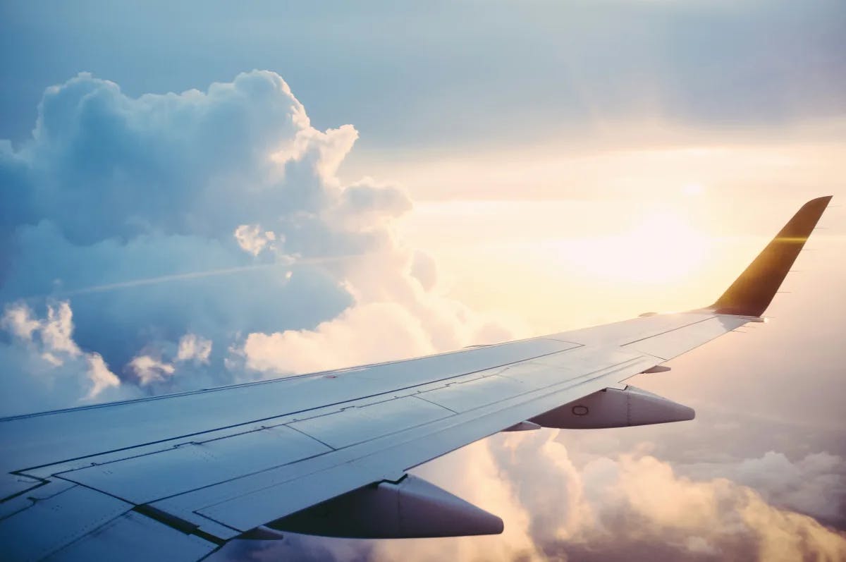 A view of an airplane wing surrounded by large white clouds and the sun shining through. 