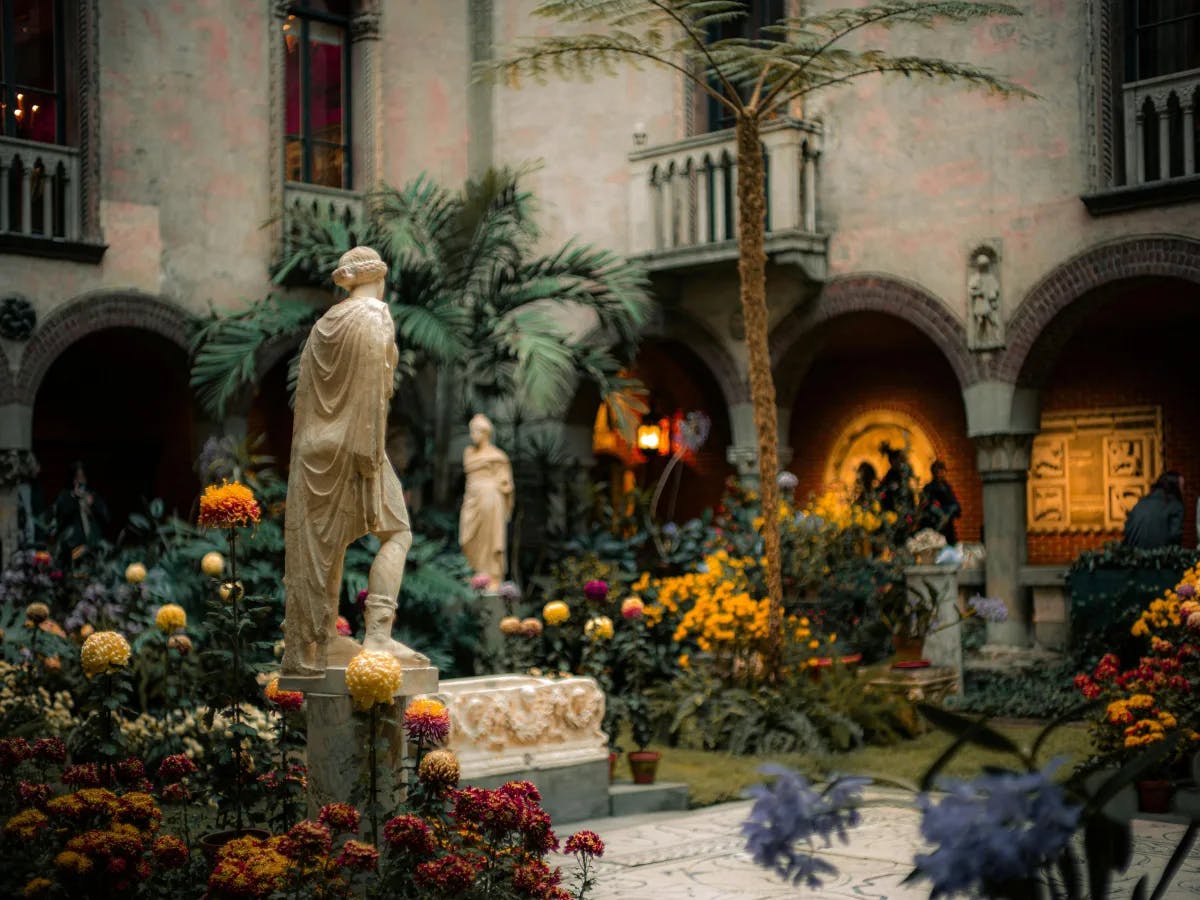 An indoor courtyard with a classical statue surrounded by lush greenery at the Isabella Stewart Gardener Museum.