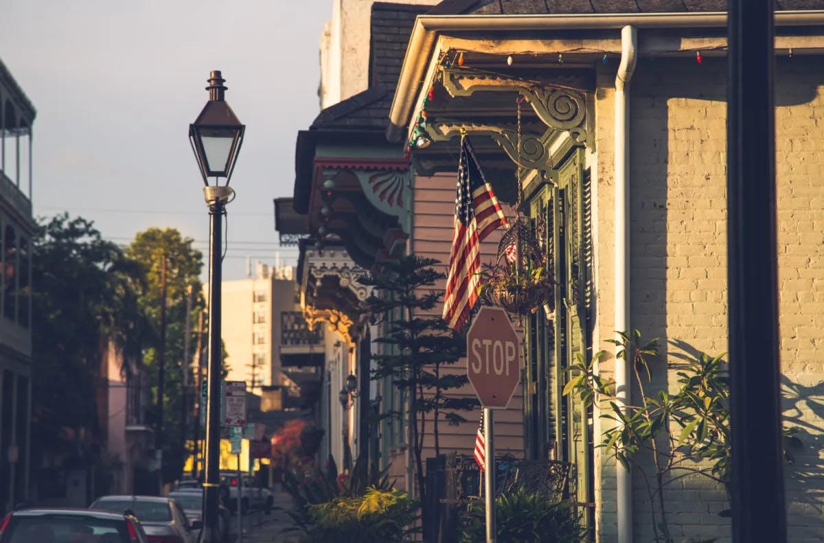 A view of a stop sign, the American flag, a stone building, street lamp and city view in the background.