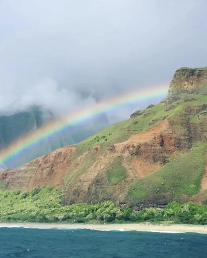 Picture of rainbow over lake at Nā Pali Coast State Wilderness Park with a shoreline and foliage. 
