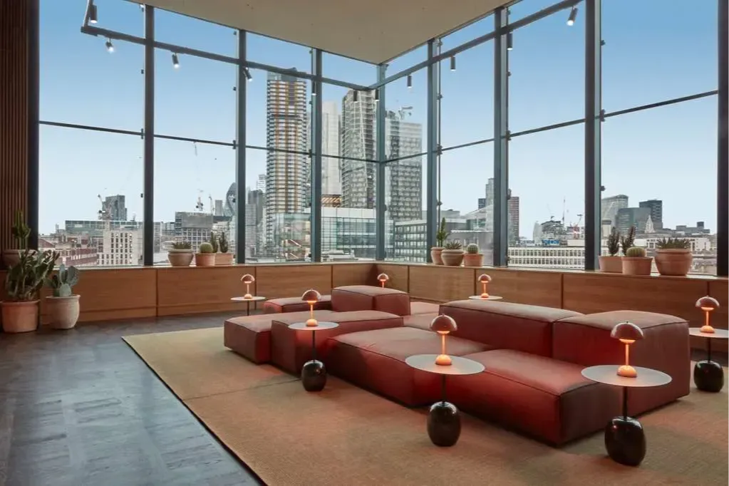 a loft with plush orange couches and floor-to-ceiling windows overlooking tall buildings