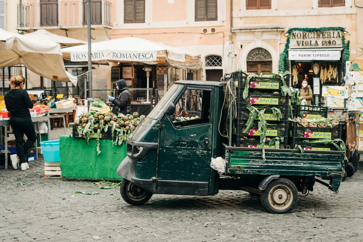 A street food market with a small green truck carrying fresh produce in Rome.