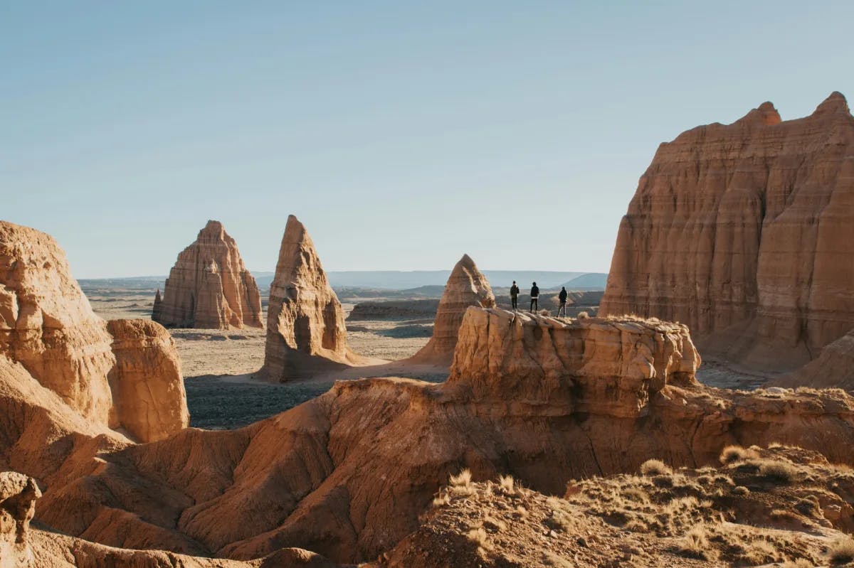 Three people standing on top of rock formations, surrounded by many towering rocks and desert.