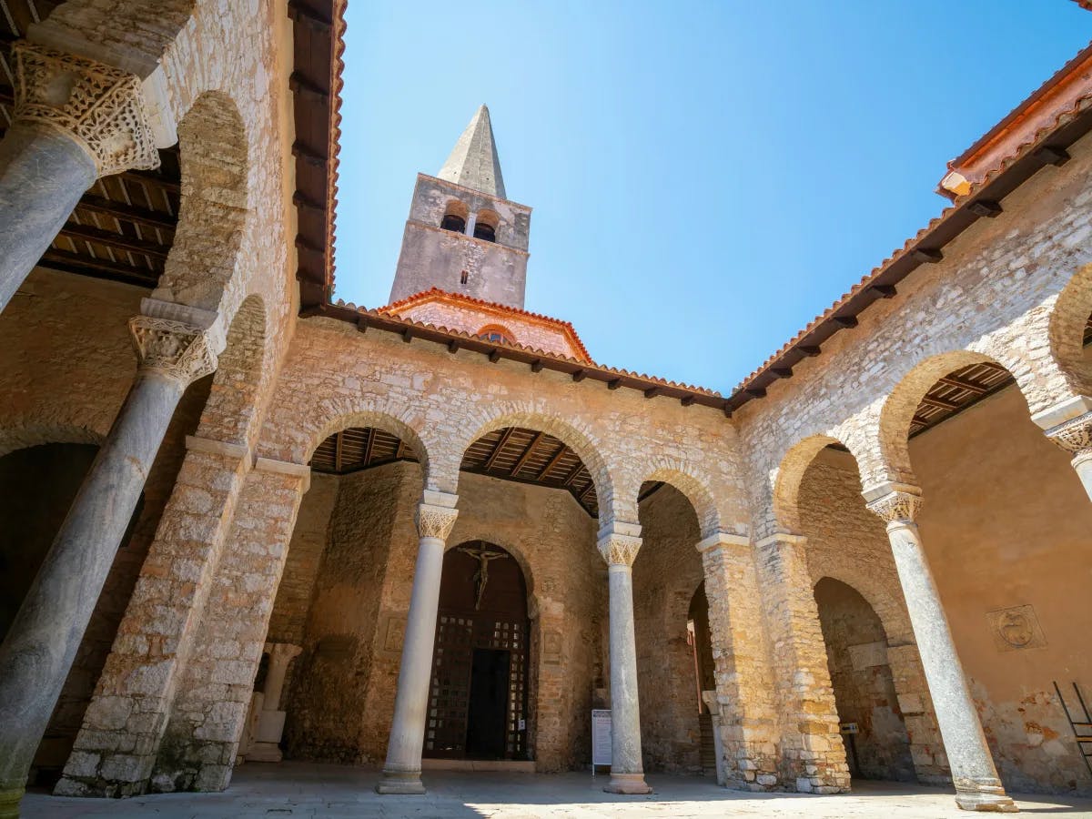 A serene courtyard with arches and a bell tower, reflecting ancient stone architecture under a clear sky.