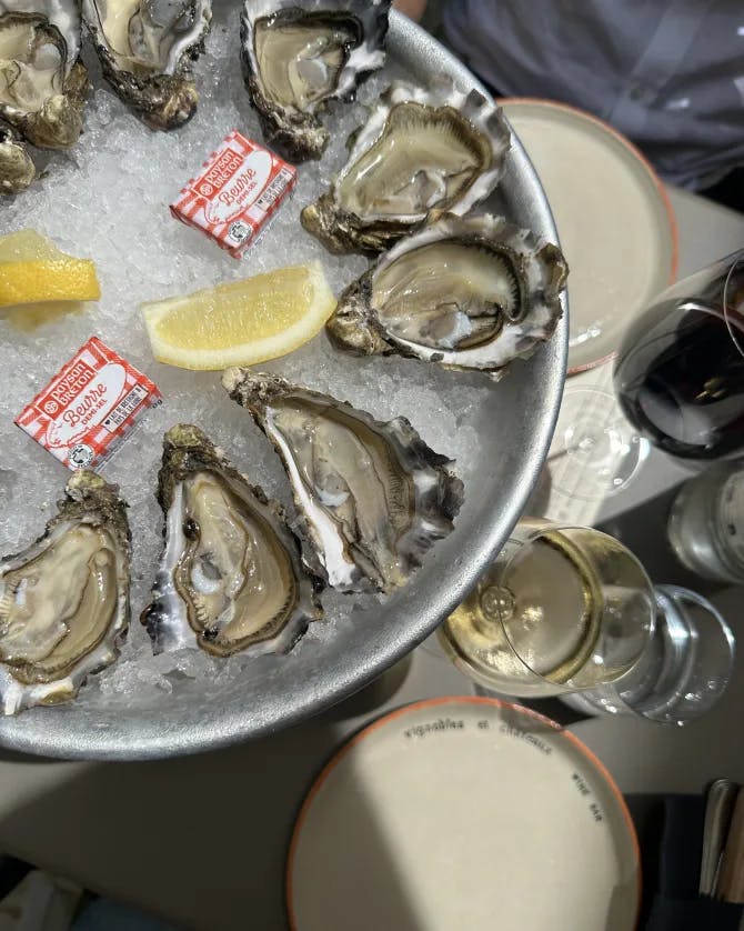 Overhead view of a tray of oysters on ice with lemon on a table with a glass of white wine