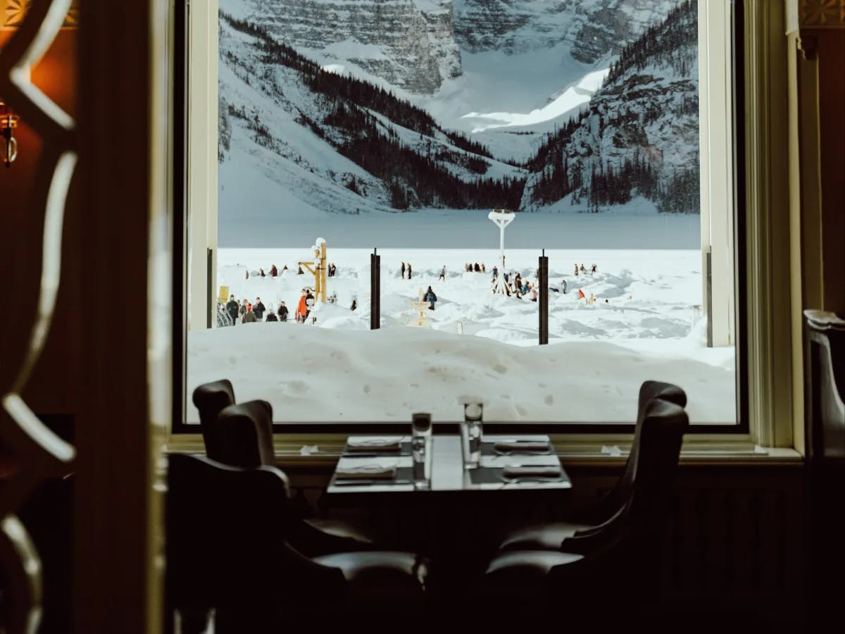 Inside of a restaurant with snowy ground and mountains views from window. 
