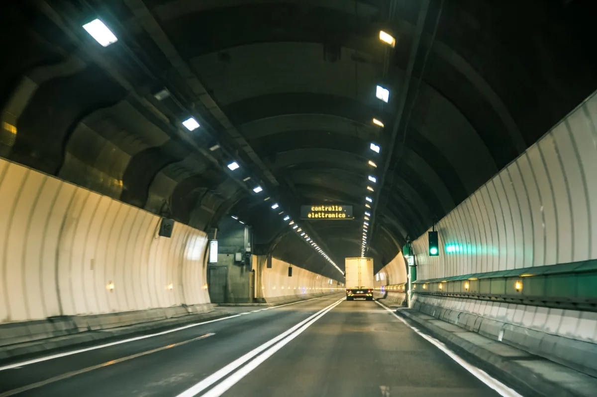 A view of the inside of a tunnel complete with paneled lighting, a green stop light, street and truck in the distance. 