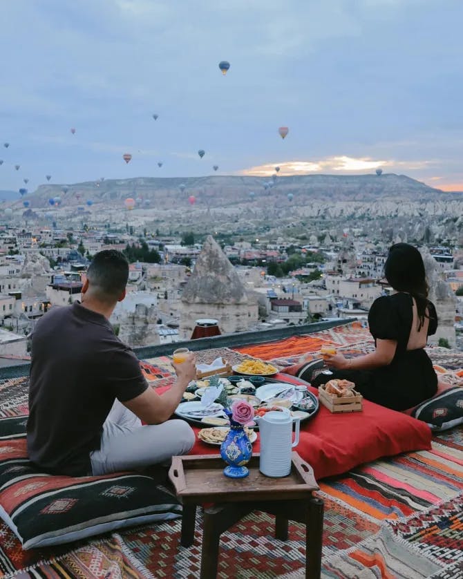 A man and woman dining on a roof top overlooking the city. 