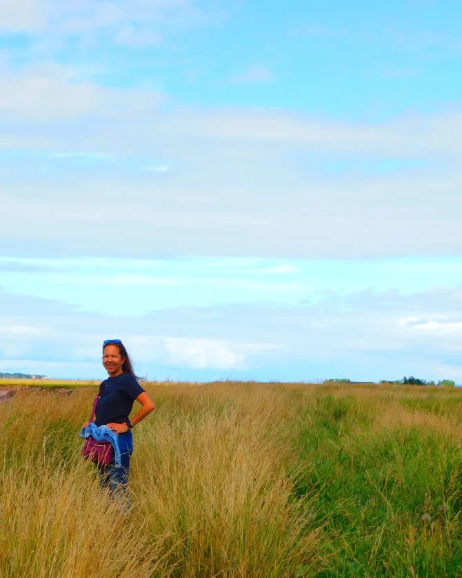 Isabel in a black shirt standing in an empty field of grass-like plants under sunny skies
