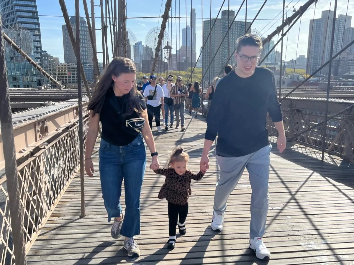 Leanne and a man walking across the Brooklyn Bridge with a little girl in between them holding their hands.