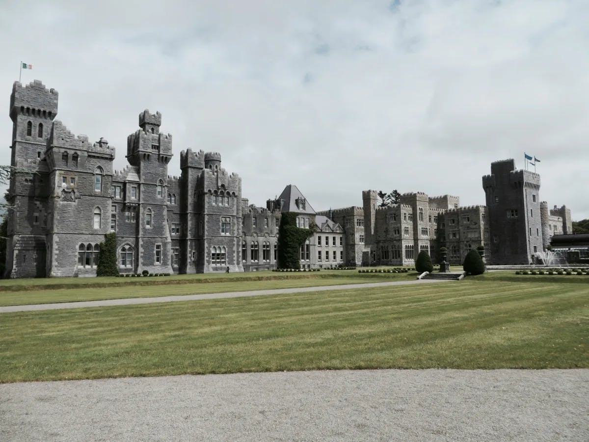 The exterior of Ashford Castle, a large gray stone campus on a lawn.