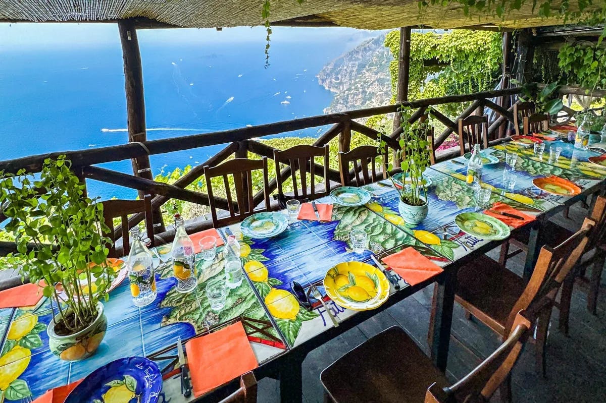 A long dining table with blue and red linens decorated with lemons overlooking the coast at La Tagliata.