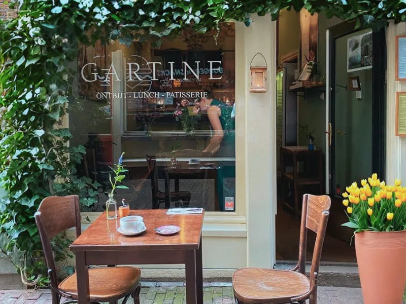 A picture of the facade of a cafe called Gartine with a small table and chairs outside and flowers decorating the exterior.