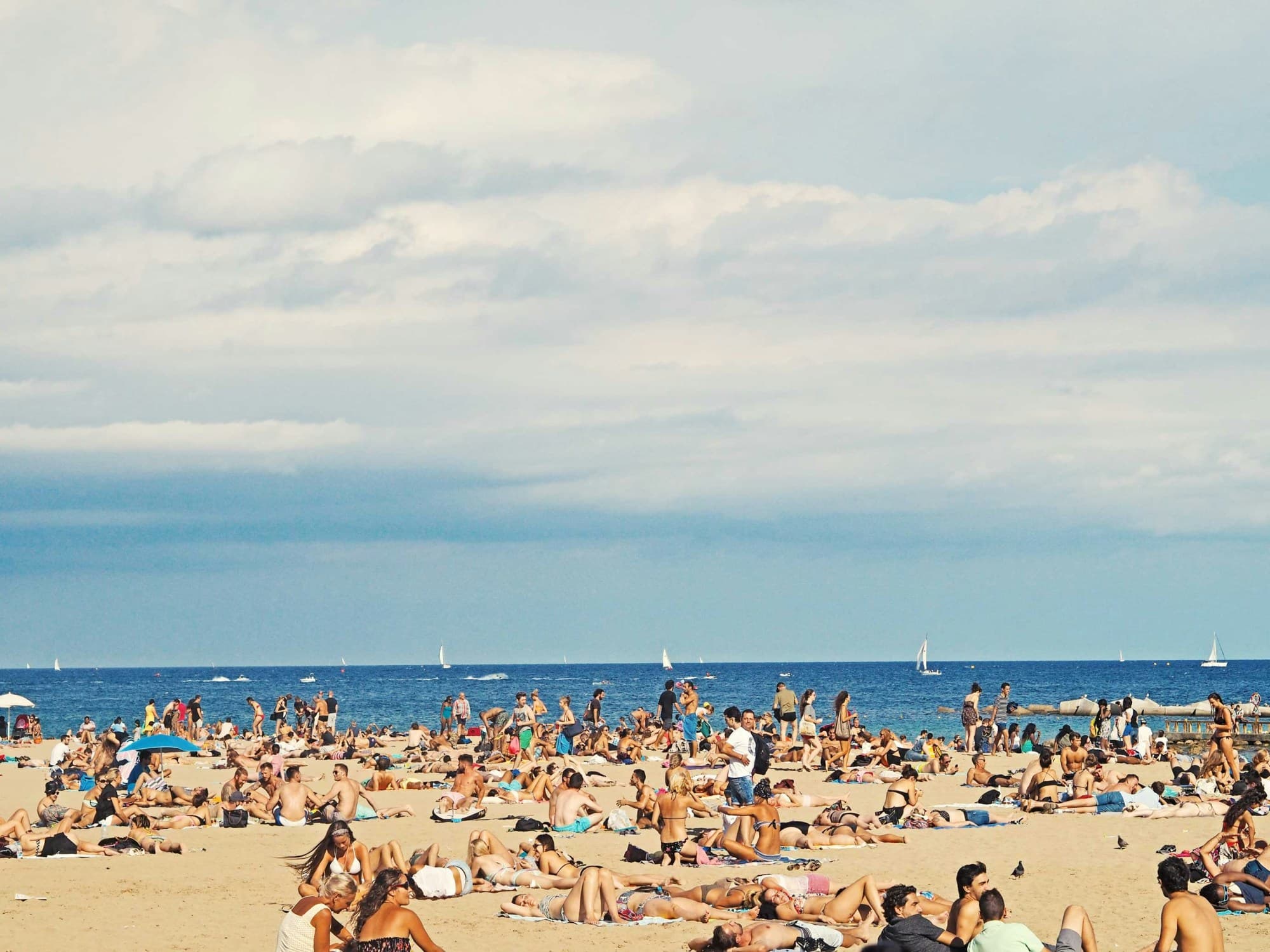 A seaside view of the beach filled with visitors on a cloudy day. 