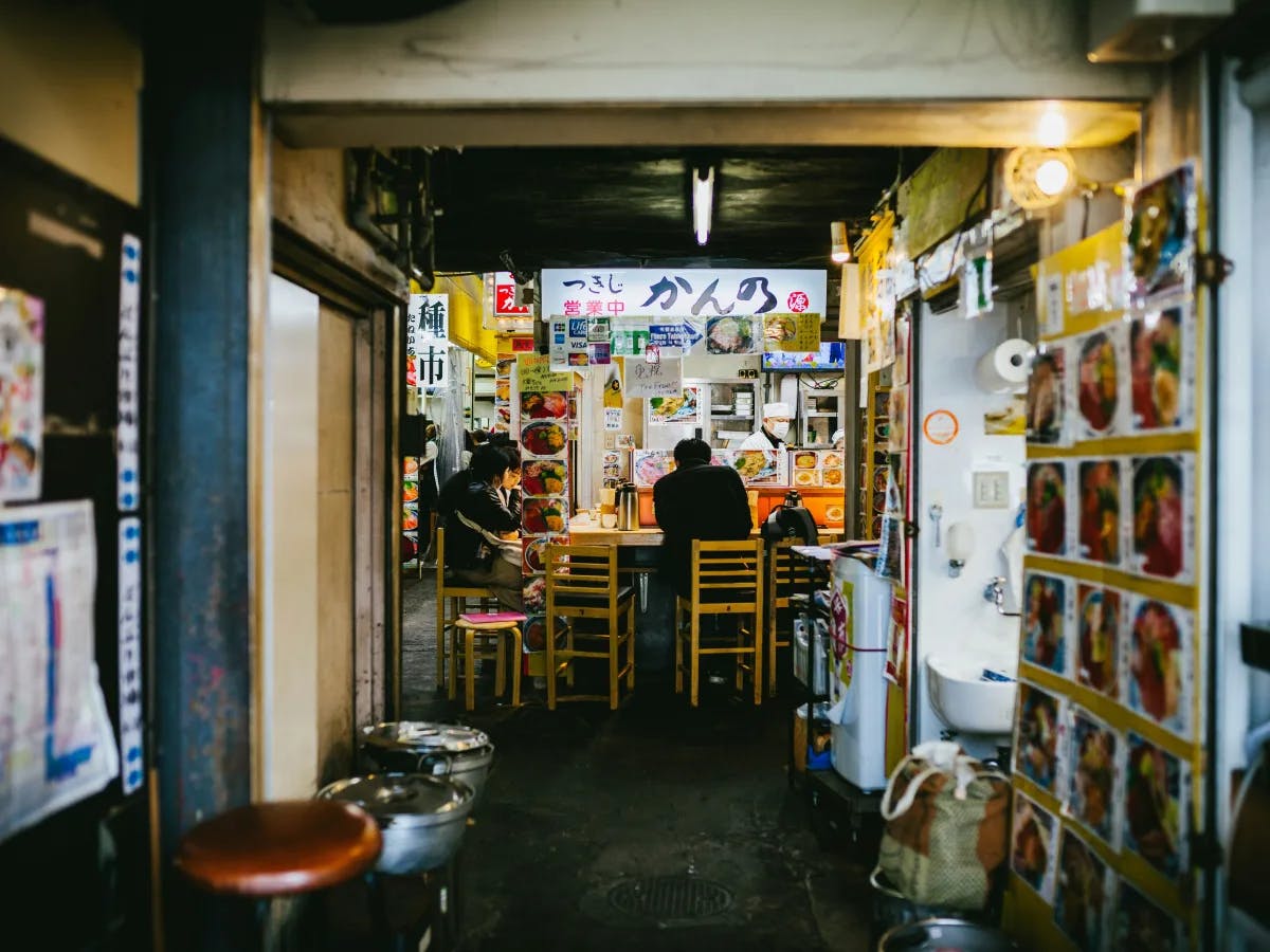 People sitting inside a food stall on wooden chairs.