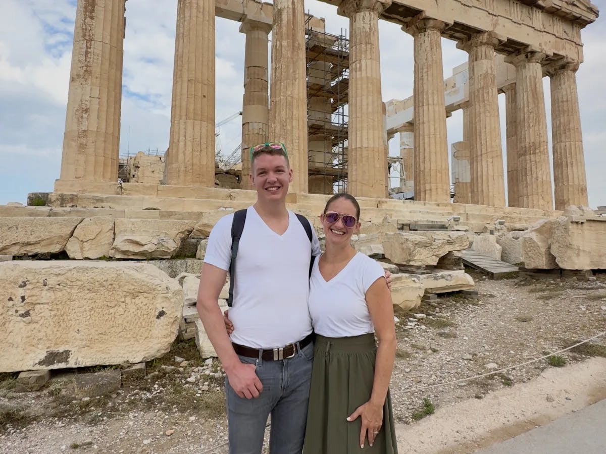 A couple standing in front of an old building ruin with pillars.