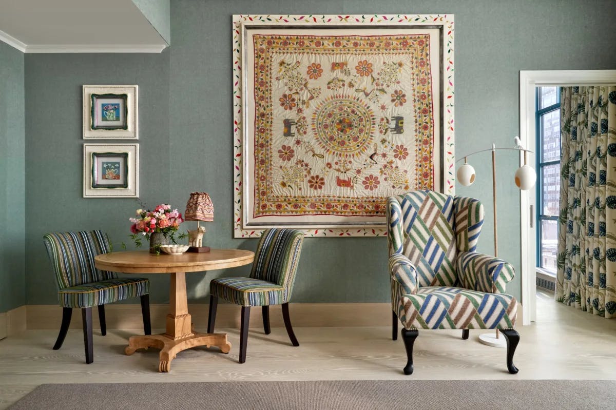 an elaborate square quilt hangs on a wall in a posh room with a zig-zag-patterned upholstered chair