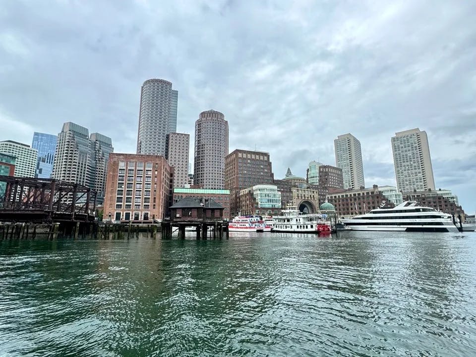 A city skyline viewed from a body of water, featuring tall buildings and cloudy skies.