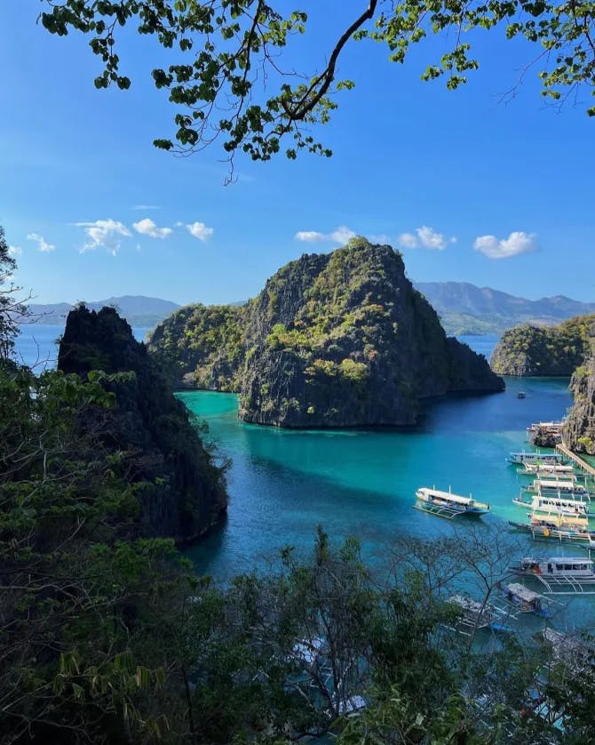 An image of the ocean on a clear day surrounded by foliage with rock formations in the distance. 