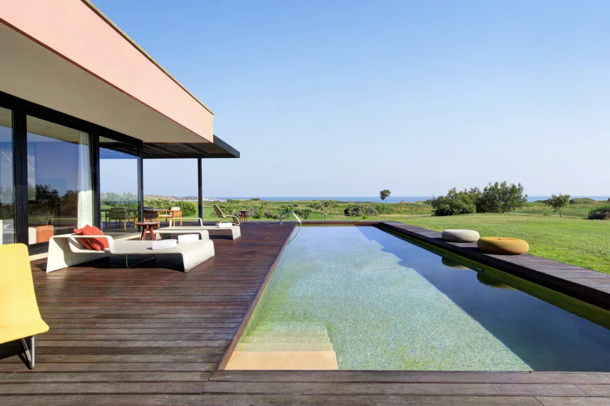 a sleek wooden deck with a rectangular infinity pool overlooking a seaside grassy expanse