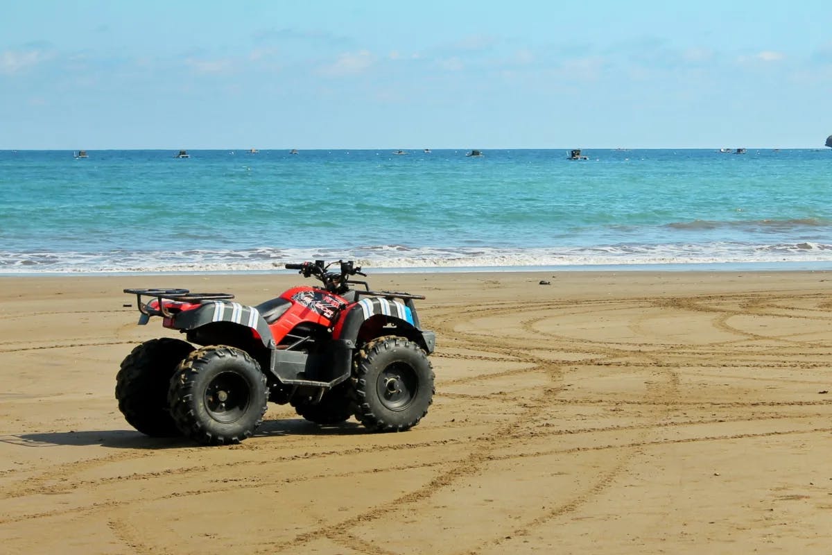 A red and black ATV parked on a beach.