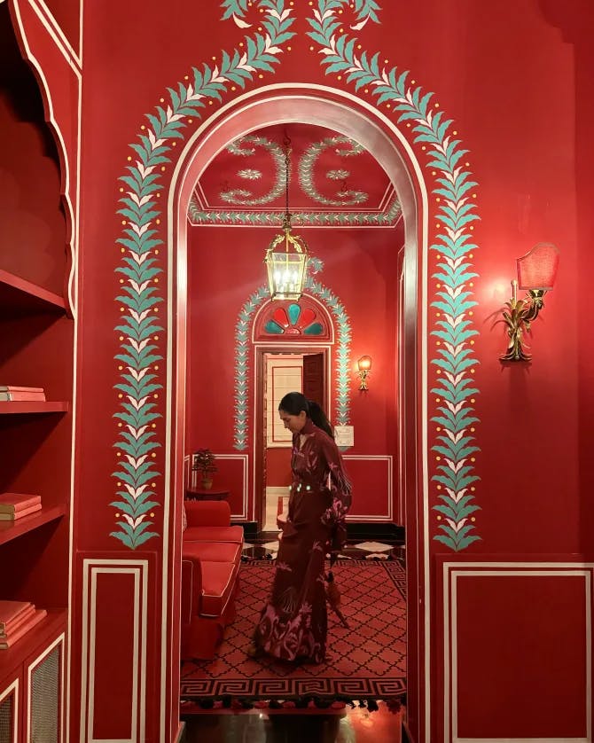 Lexi posing in a red dress, standing the doorway of a red room / lobby at the Villa Palladio Jaipur, in India.