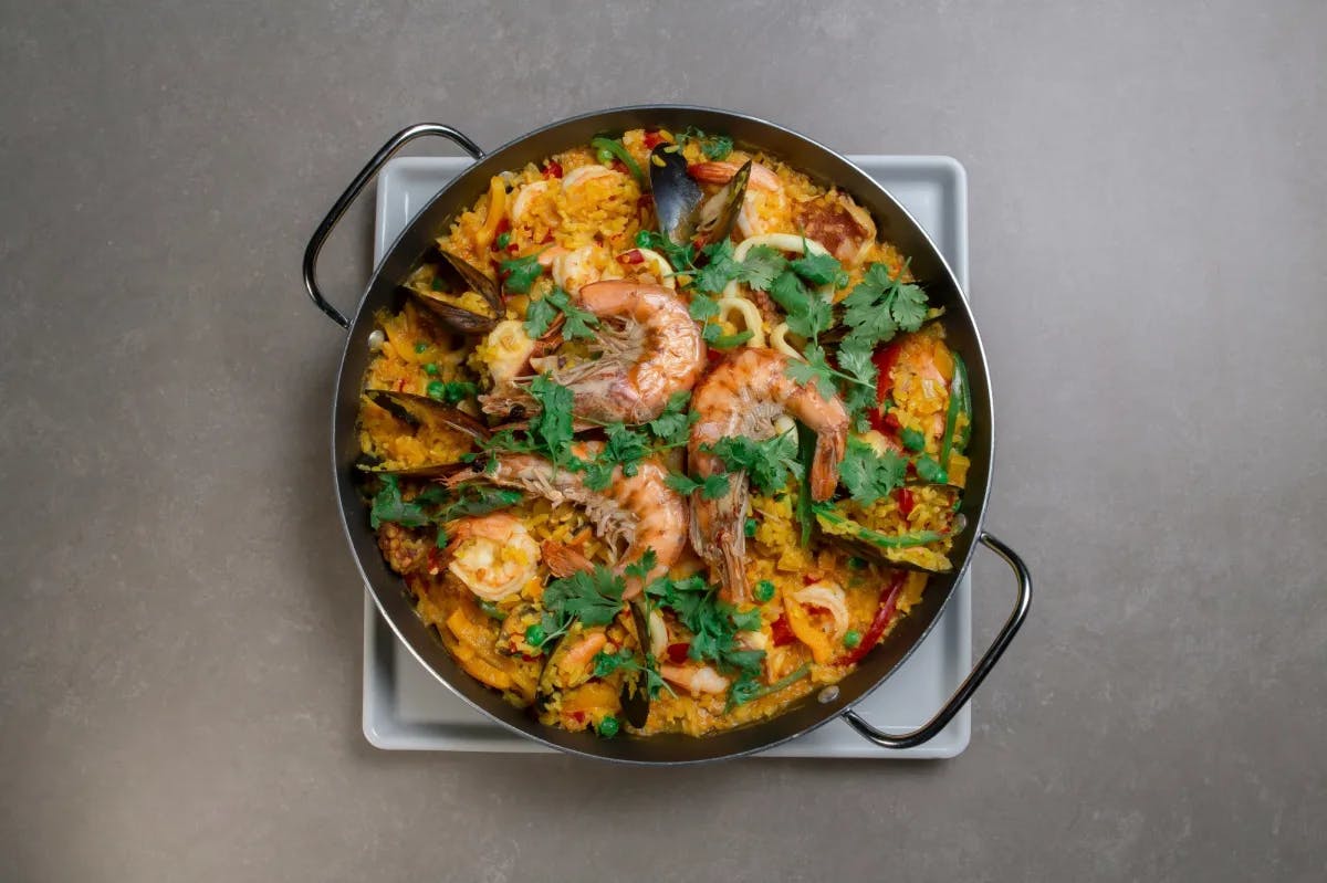 This image depicts a pan full of paella on top of a blank countertop. 