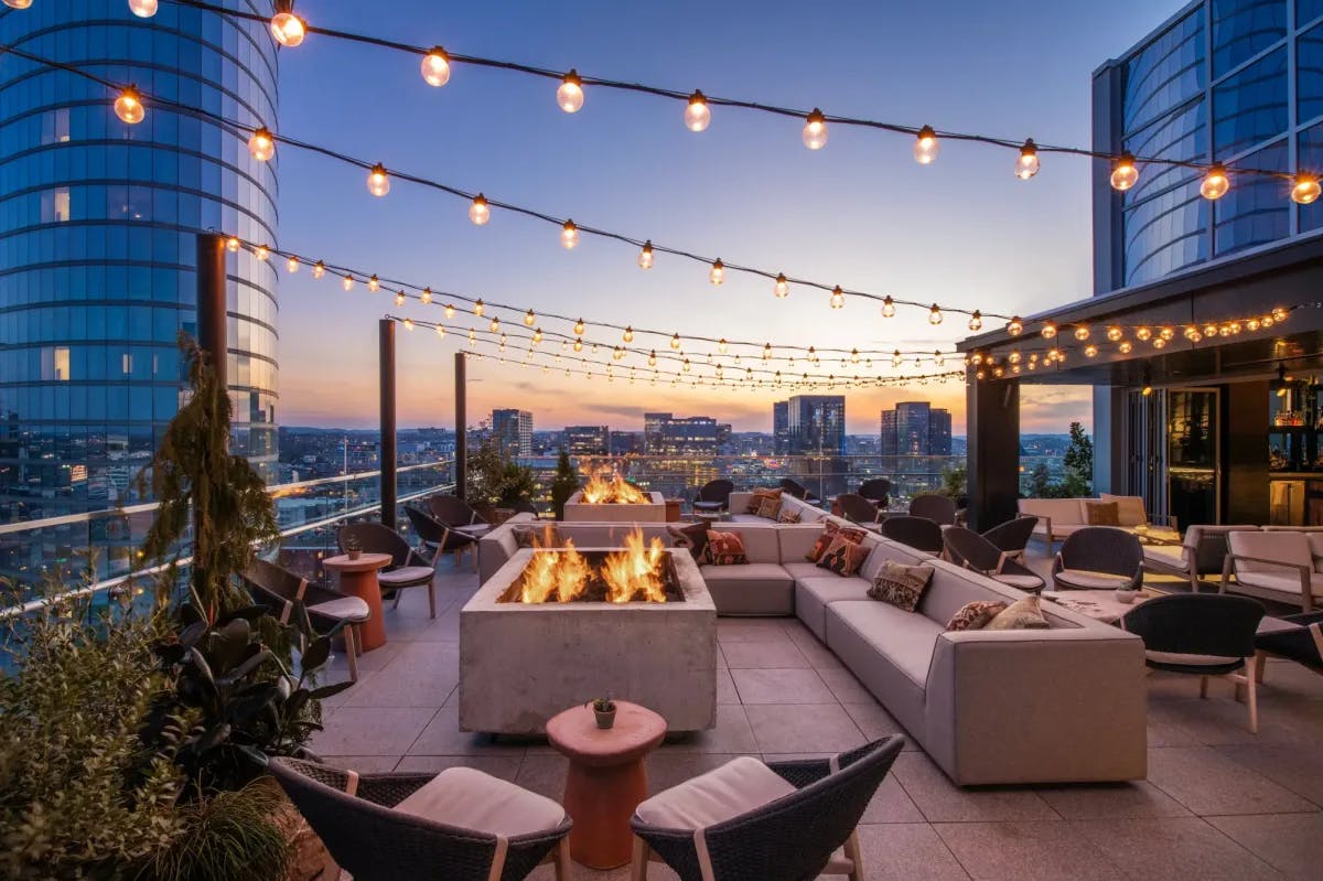 Chic rooftop lounge with string lighting, firepits and comfy outdoor seating with an excellent view of Downtown Nashville