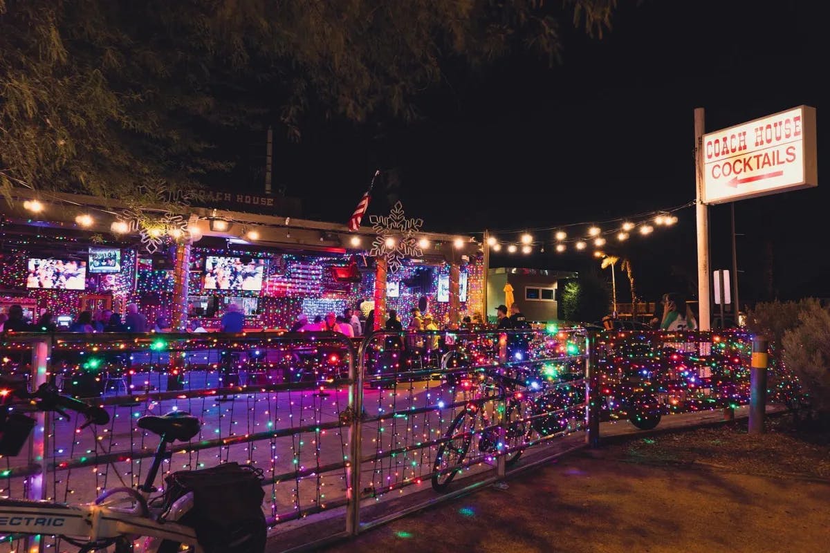 A fence wrapped in string lights in front of a bar at nightime